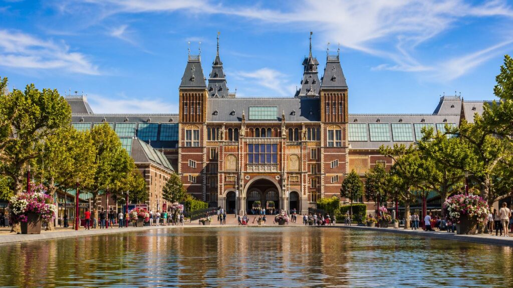 Buitenkant van het Rijksmuseum in Amsterdam met water, bomen en bezoekers op het Museumplein.